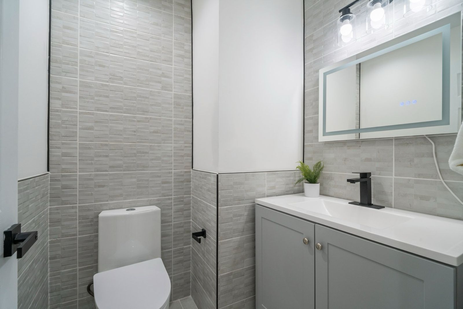 Finished powder room in a Gwynn Oak, Baltimore County home with gray stacked tile, floating vanity, LED mirror and matte black fixtures