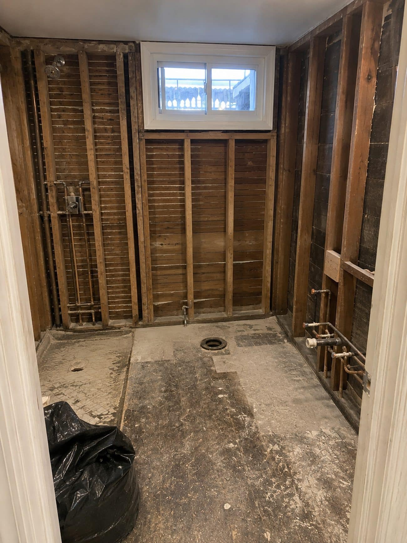 Basement bathroom gutted to bare studs and lath showing original copper supply lines
