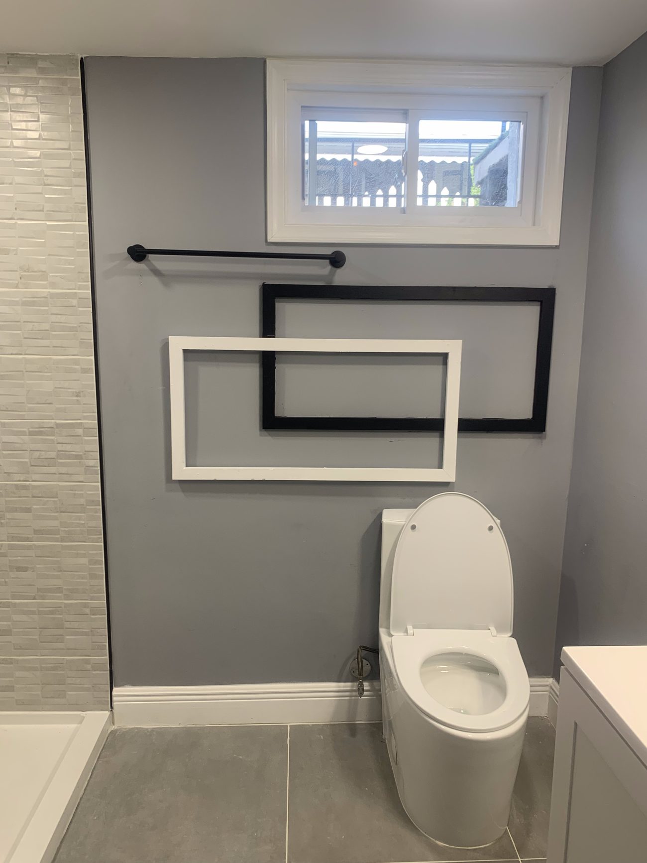 Finished basement bathroom with gray walls, tile accent wall and new toilet below the window