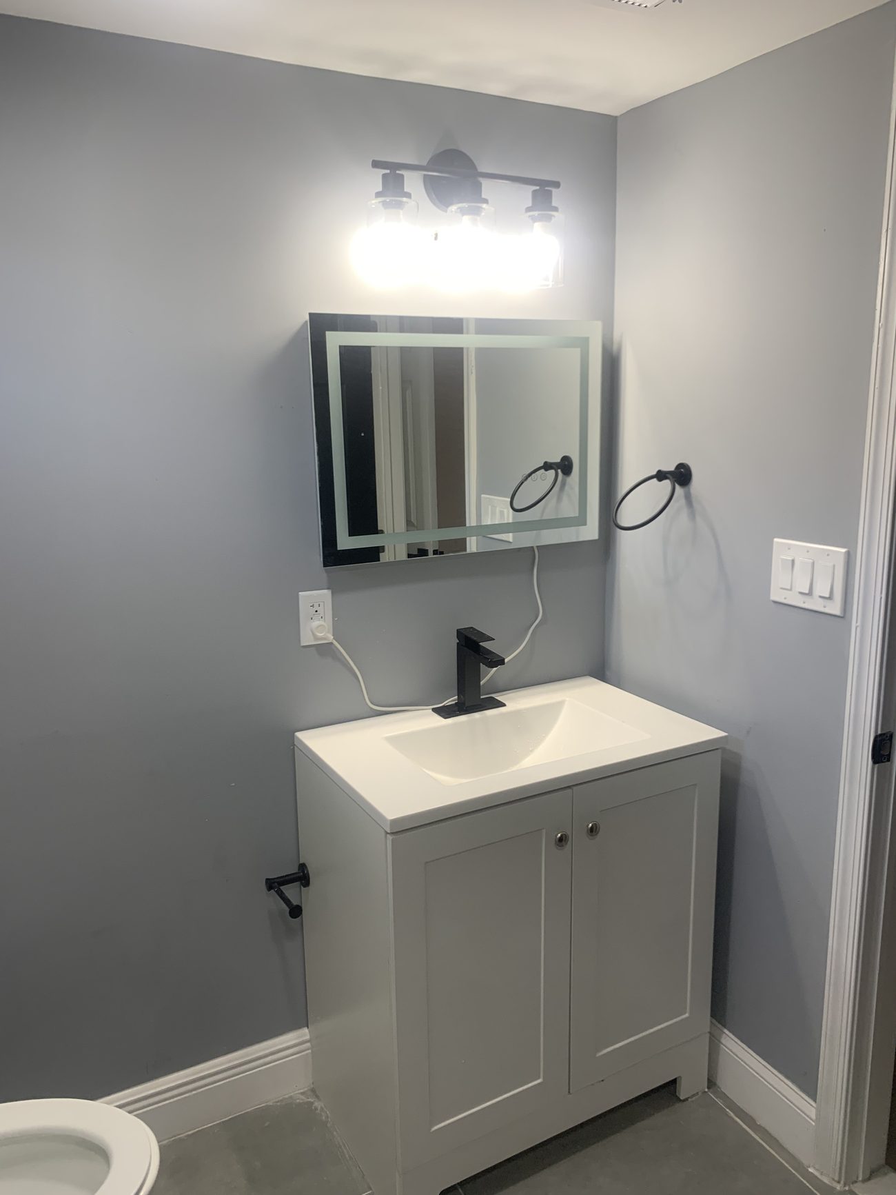 Finished basement bathroom vanity with lighted mirror and matte black faucet