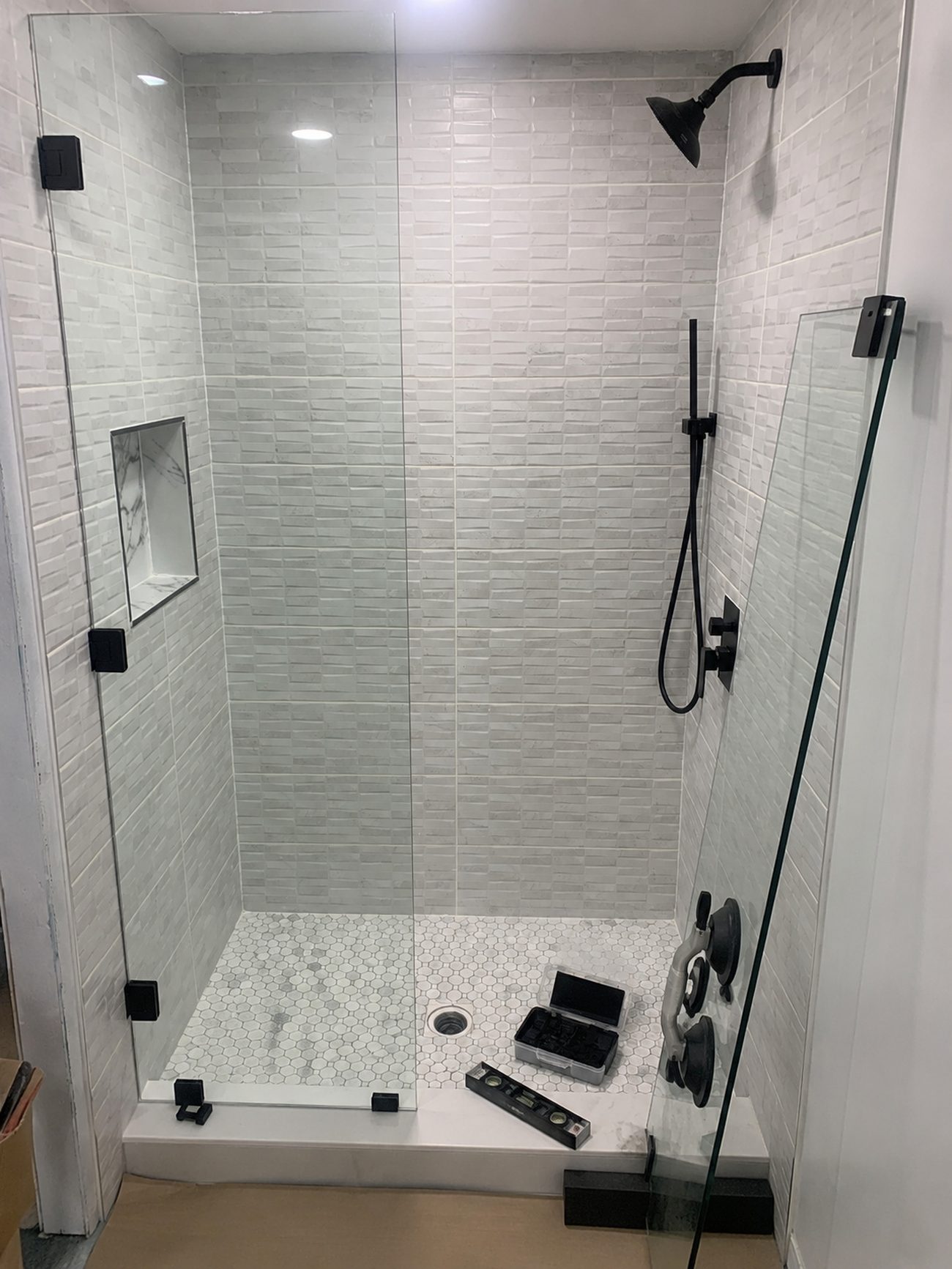 Finished basement shower with frameless glass panel, gray tile and hex mosaic floor