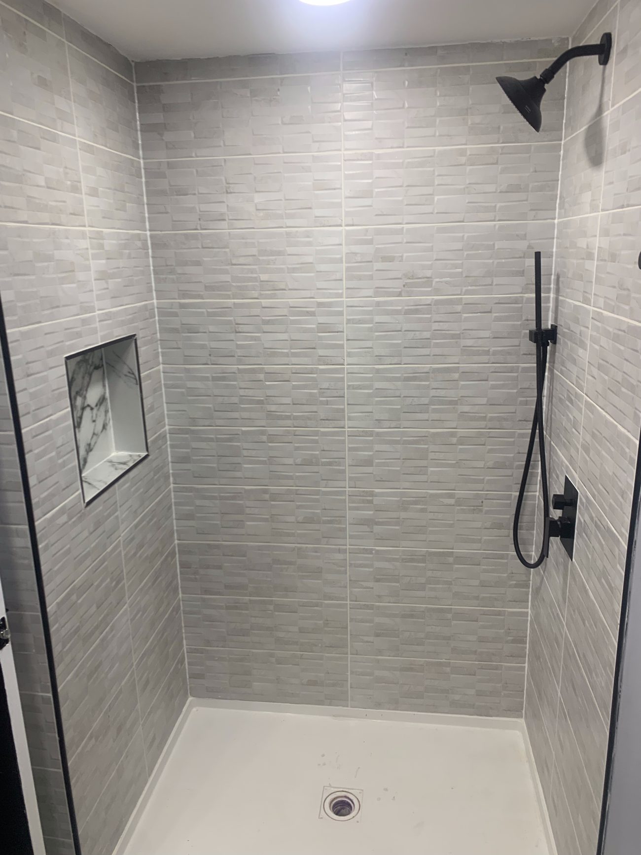 Finished basement shower with gray stacked tile, marble niche and matte black fixtures