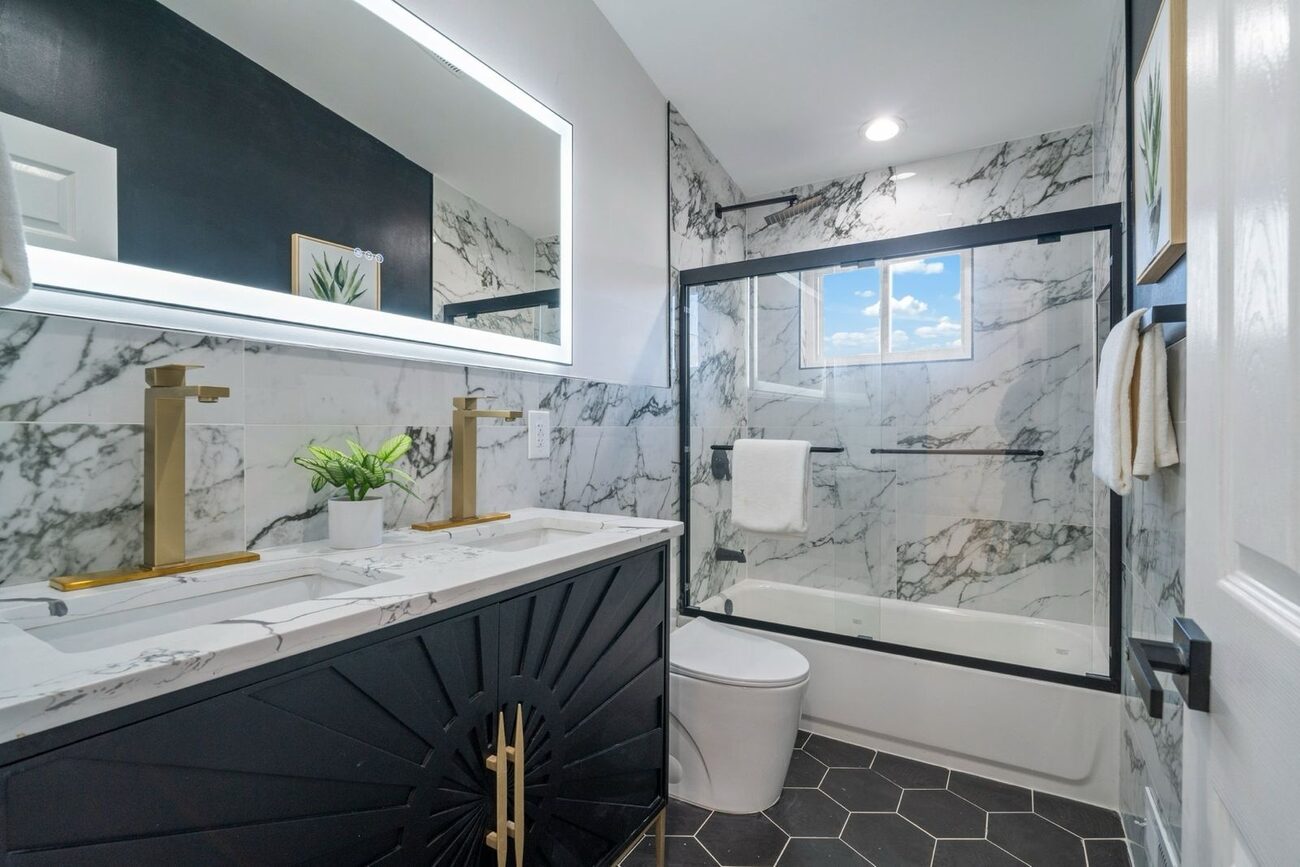Finished full bathroom with navy vanity, gold fixtures, marble tile walls and a tub