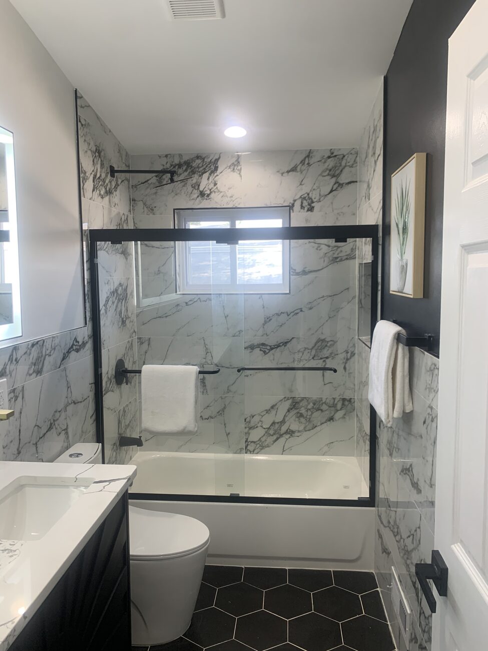 Finished full bathroom with marble-look tile walls and a black framed glass shower enclosure